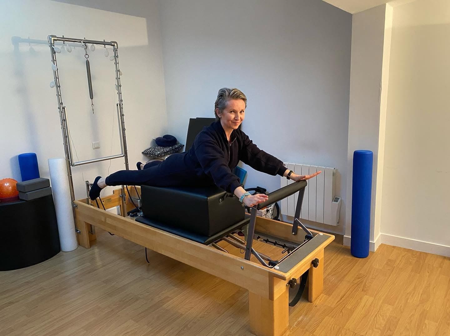 Nataliya Yefimova allongée sur le Reformer du studio, jambes tendues, mains sur la barre, sourire à l’objectif.