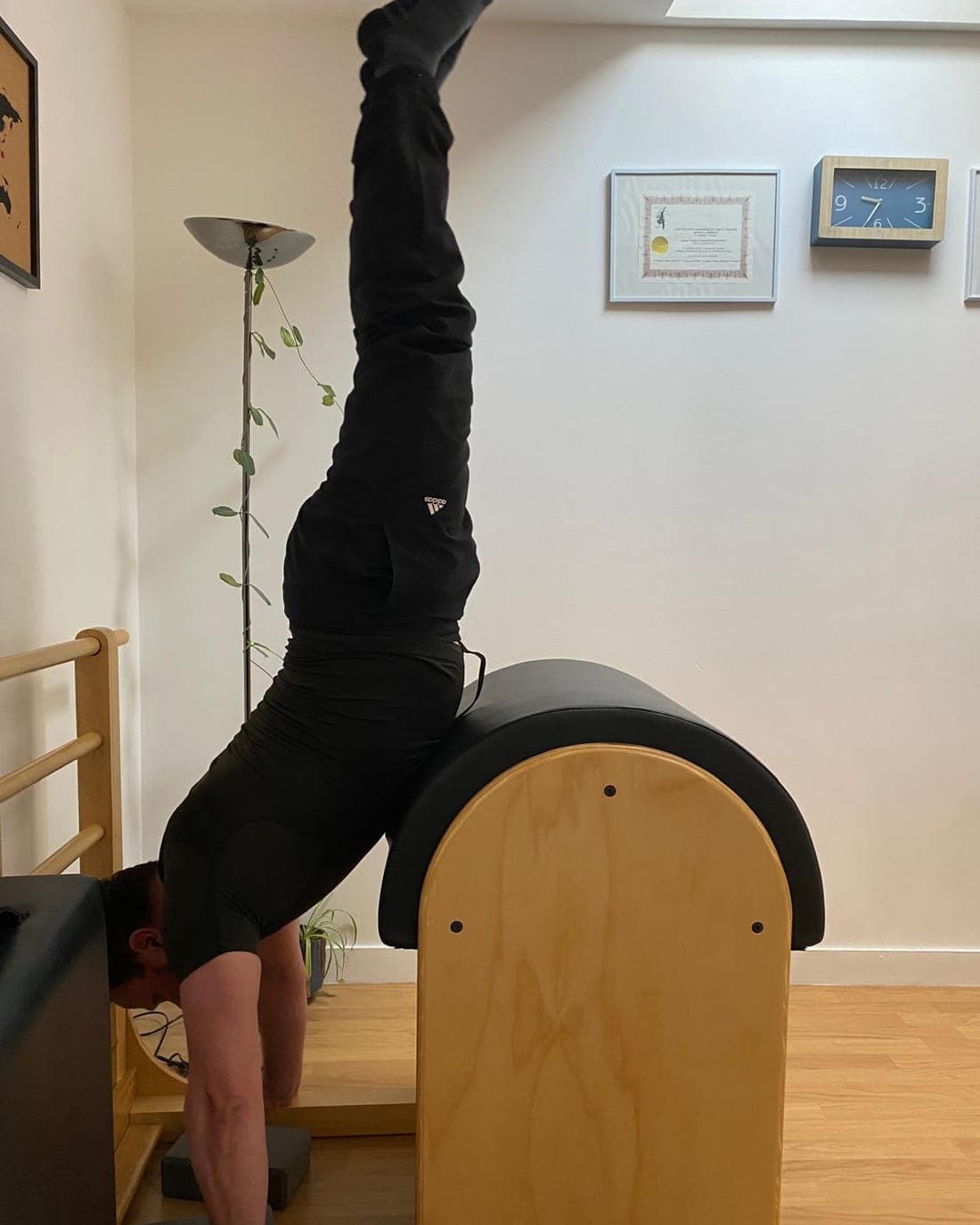 Position inversée sur le Barrel du studio : mains en appui au sol, bassin posé sur le coussin, jambes tendues à la verticale, à côté d’une échelle de bois.